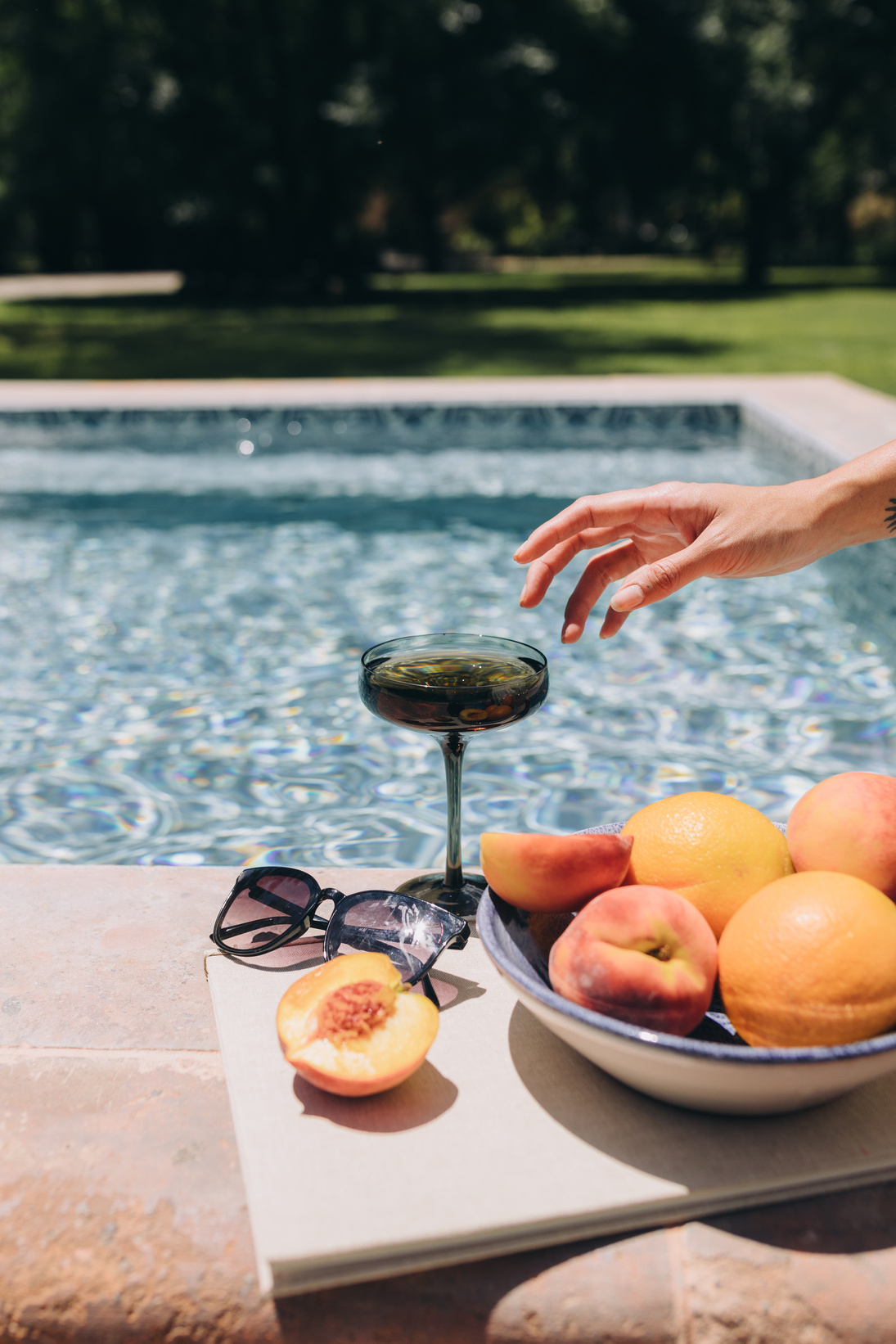 Person's Hand Reaching for Wine and Peaches by the Pool